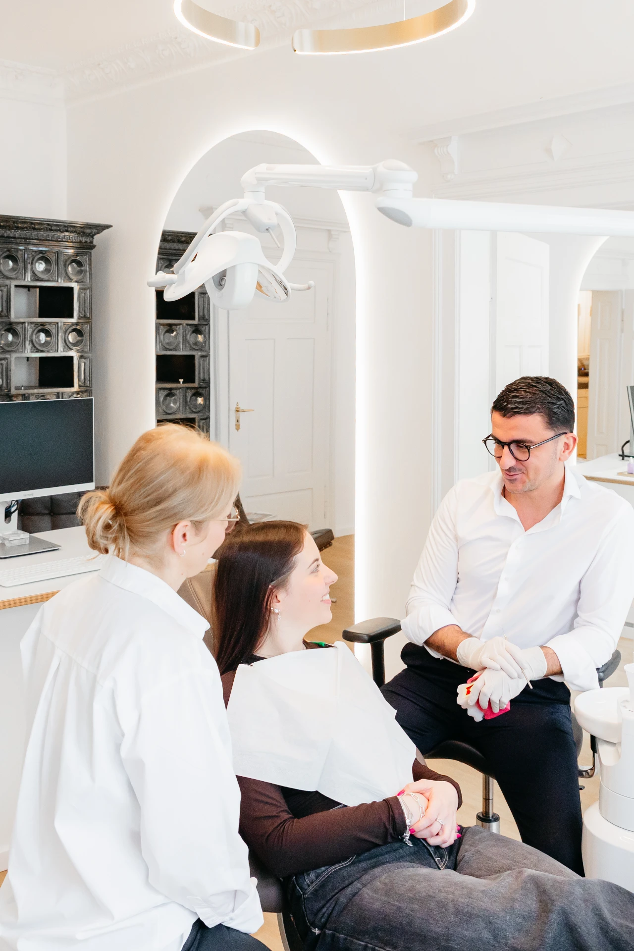 zahnarzt-oberholzer_schwabing_beratungsgespraech-behandlungsraum_hoch Beratungsgespräch zwischen Zahnarzt-Team und Patientin im Behandlungsraum der Praxis Dr. Oberholzer Schwabing