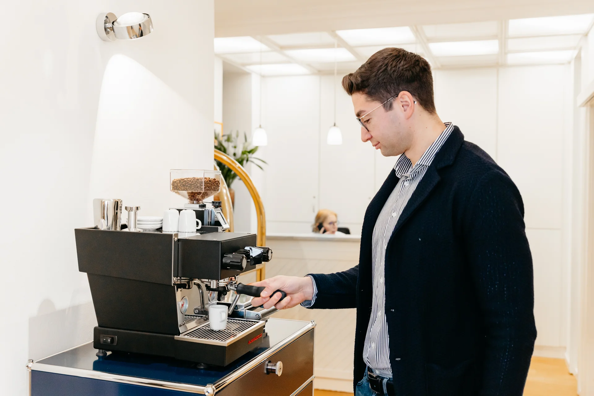 zahnarzt-oberholzer_schwabing_kaffeebar-patient Patient bereitet sich einen Kaffee an der Siebträgermaschine in der Zahnarztpraxis Dr. Oberholzer Schwabing zu